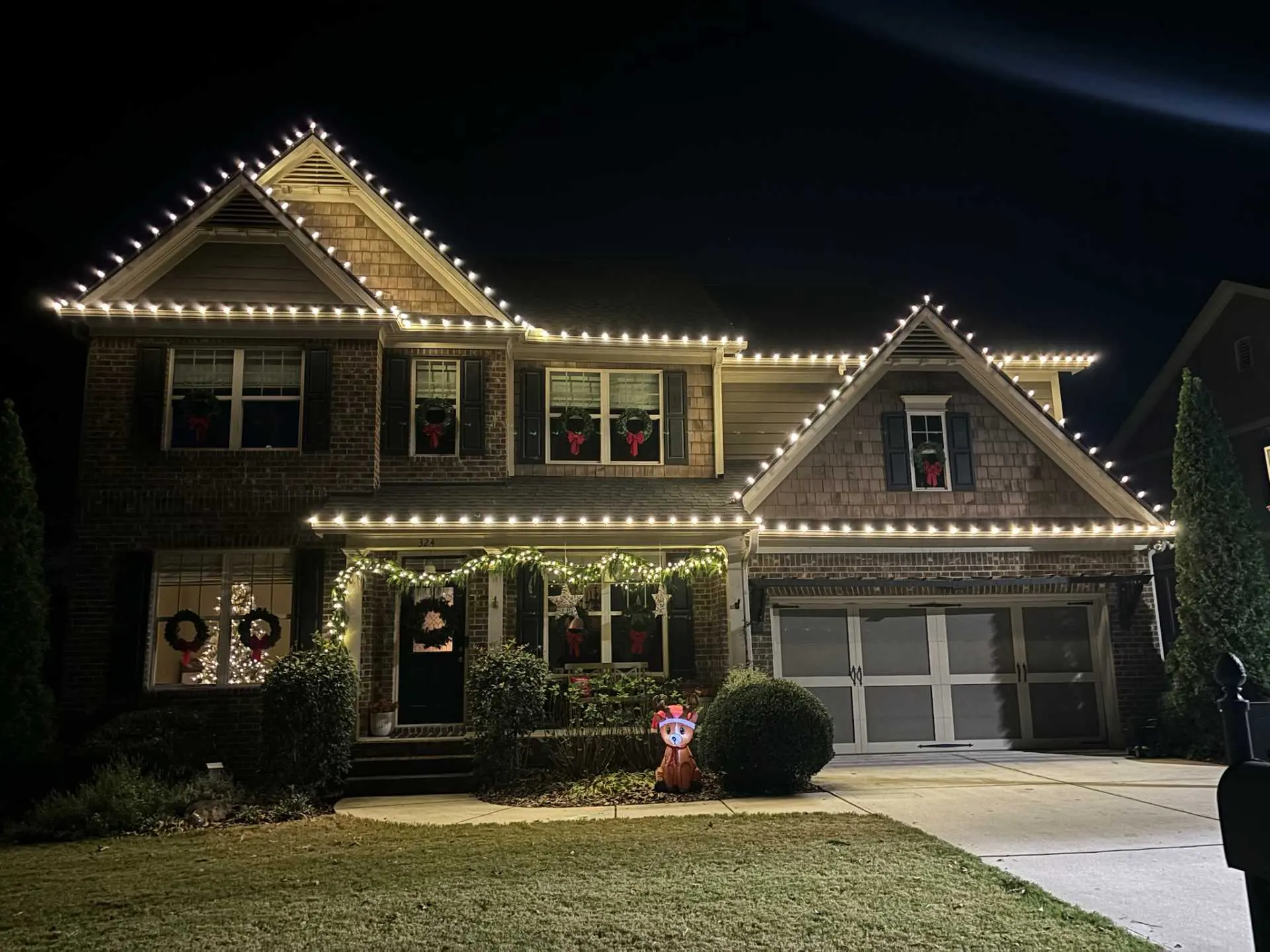 Warm white roofline Christmas lights with wreaths and exterior decorations on a residential property in Cumming, Georgia.