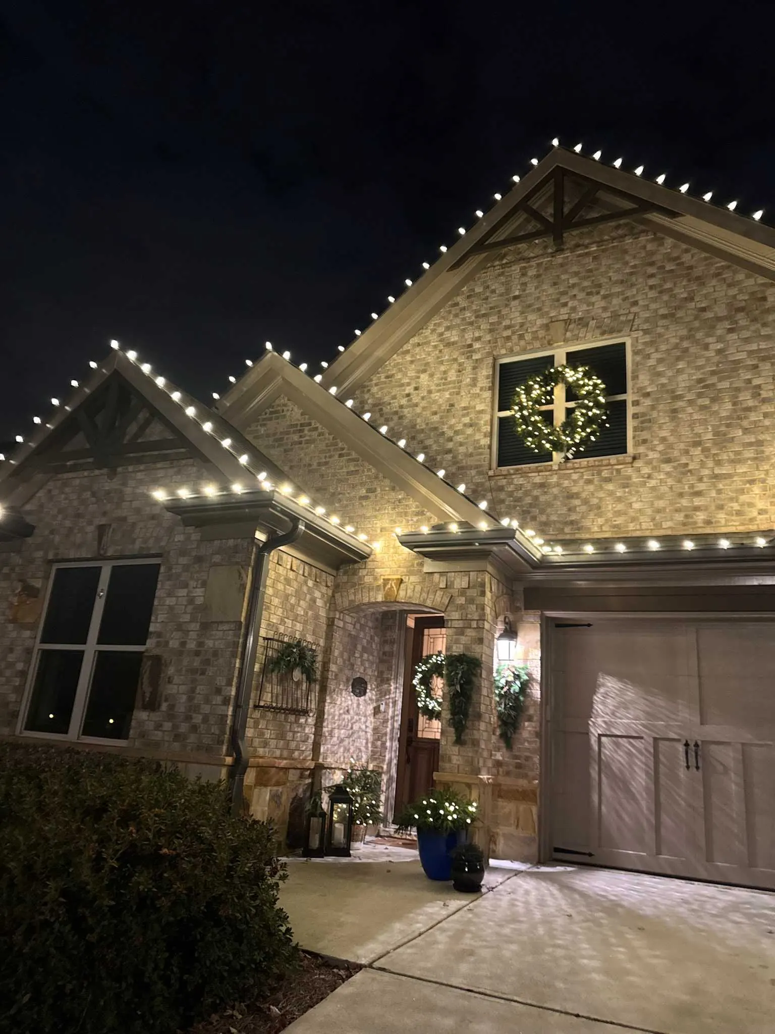 Warm white roofline Christmas lights and a lit wreath decorating a residential entry in Cumming, Georgia.